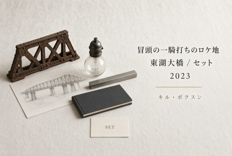 象牙色の布の上に、錆びたトラスの模型、鉄橋の鉛筆スケッチ、スタジオ用の電球、細い鋼材、閉じた黒いノート、SETと印刷したカード。右に「冒頭の一騎打ちのロケ地／東湖大橋 / セット／2023／キル・ボクスン」。人物はいない。